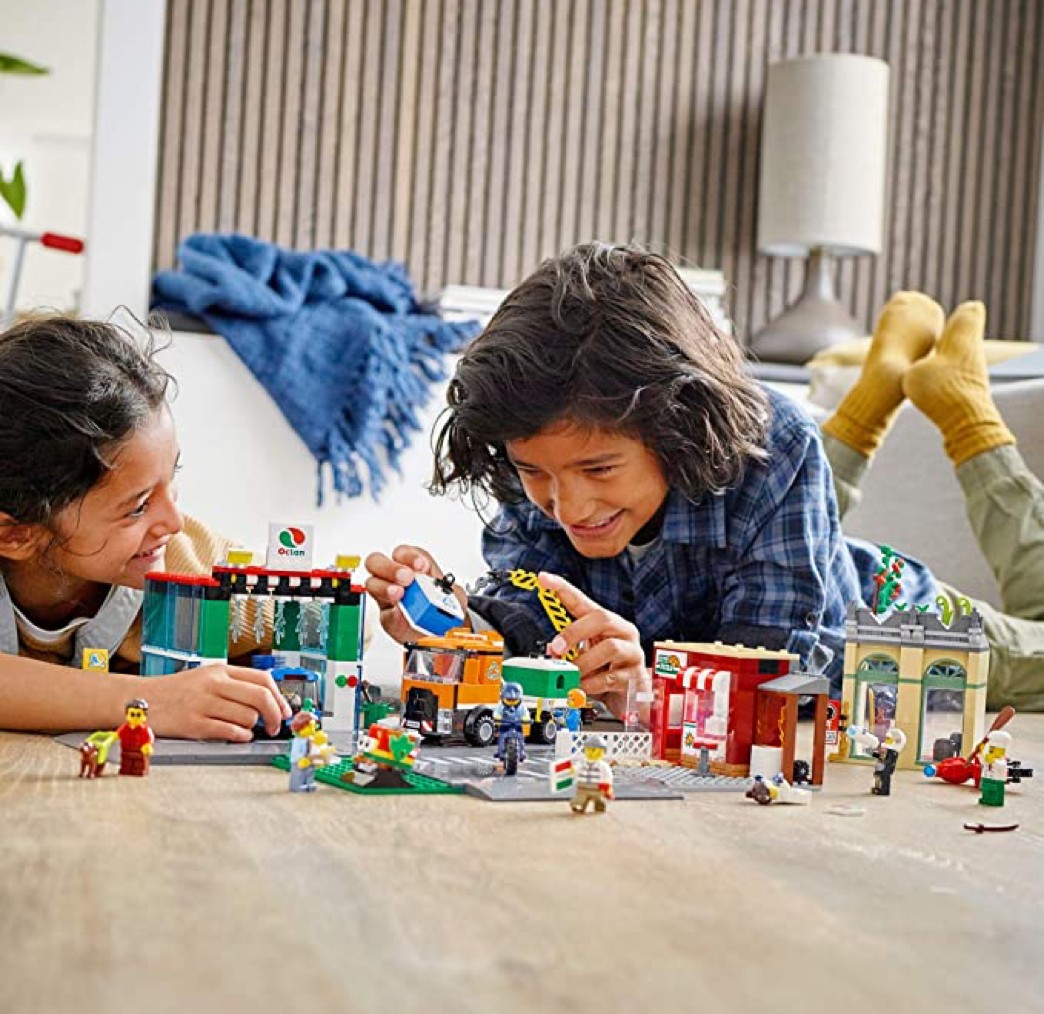 Two smiling kids playing with Lego structure that is built on the floor
