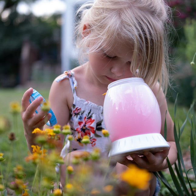 From Fat Brain Toys: Young child playing with Buggy Light, an insect viewing toy, outside with flowers in foreground.