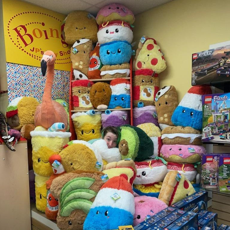 Store display filled with various Squishables comfort food toys, with person hiding in the middle